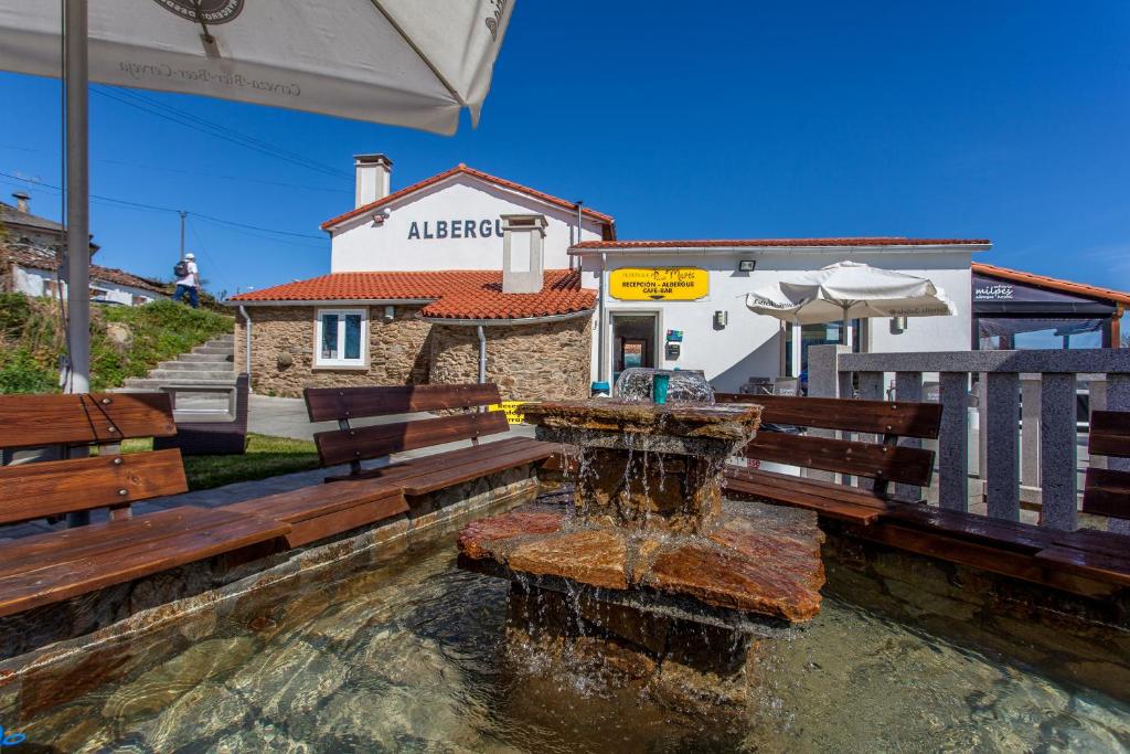 una fuente de agua frente a un edificio con bancos en Albergue Milpés, en Ribadiso