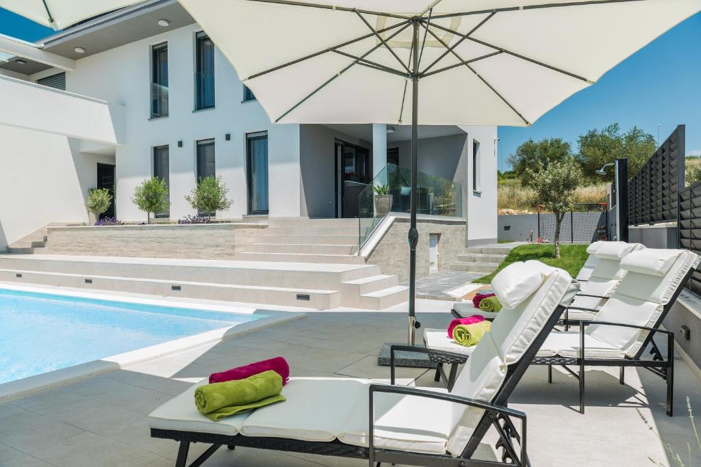 patio z krzesłami i parasolem przy basenie w obiekcie Villa Franica Zadar w mieście Zadar