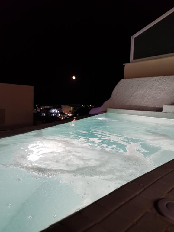 a hot tub on the roof of a building at night at Amera Suites in Fira