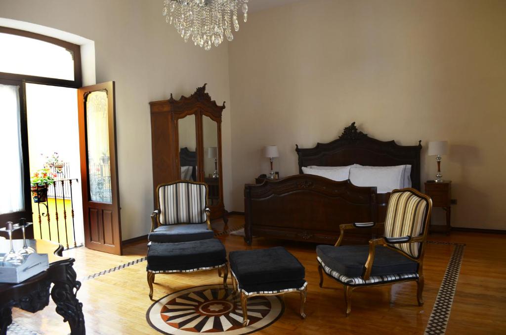 a bedroom with a bed and two chairs and a chandelier at Hotel Marqués del Ángel in Puebla