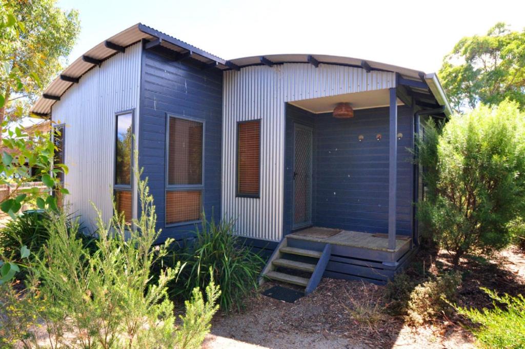 a blue tiny house with a porch and stairs at BEACHCROFT - INLET SIDE in Inverloch