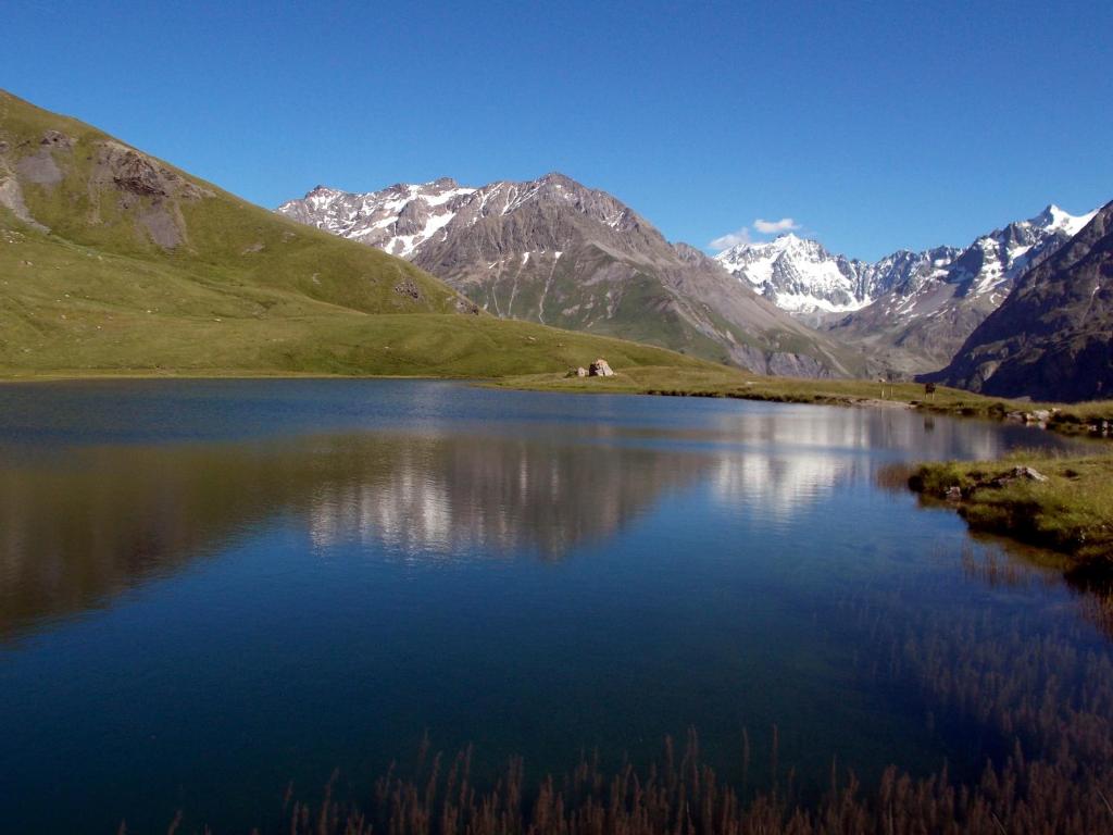 a mountain lake with snow capped mountains in the background at Hotel Le Faranchin in Villar-dʼArène