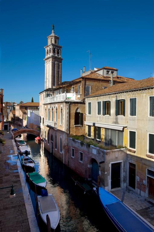 a group of boats in a canal with a clock tower at Hotel Pausania in Venice