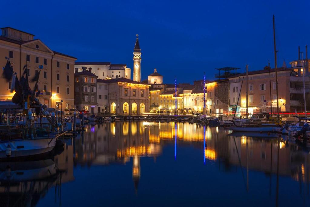 eine Stadt in der Nacht mit einem Uhrturm im Hintergrund in der Unterkunft Galilea 14 in Piran