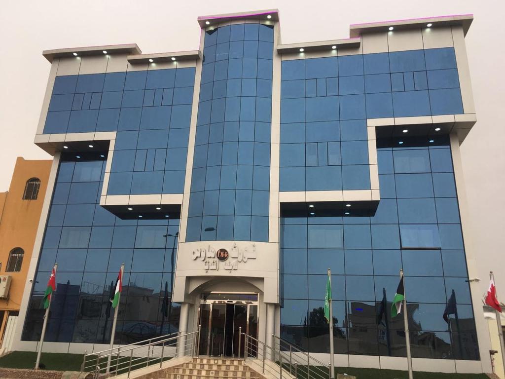 un edificio di vetro alto con bandiere di fronte di Nourth House ApartHotel a Al Qurayyat