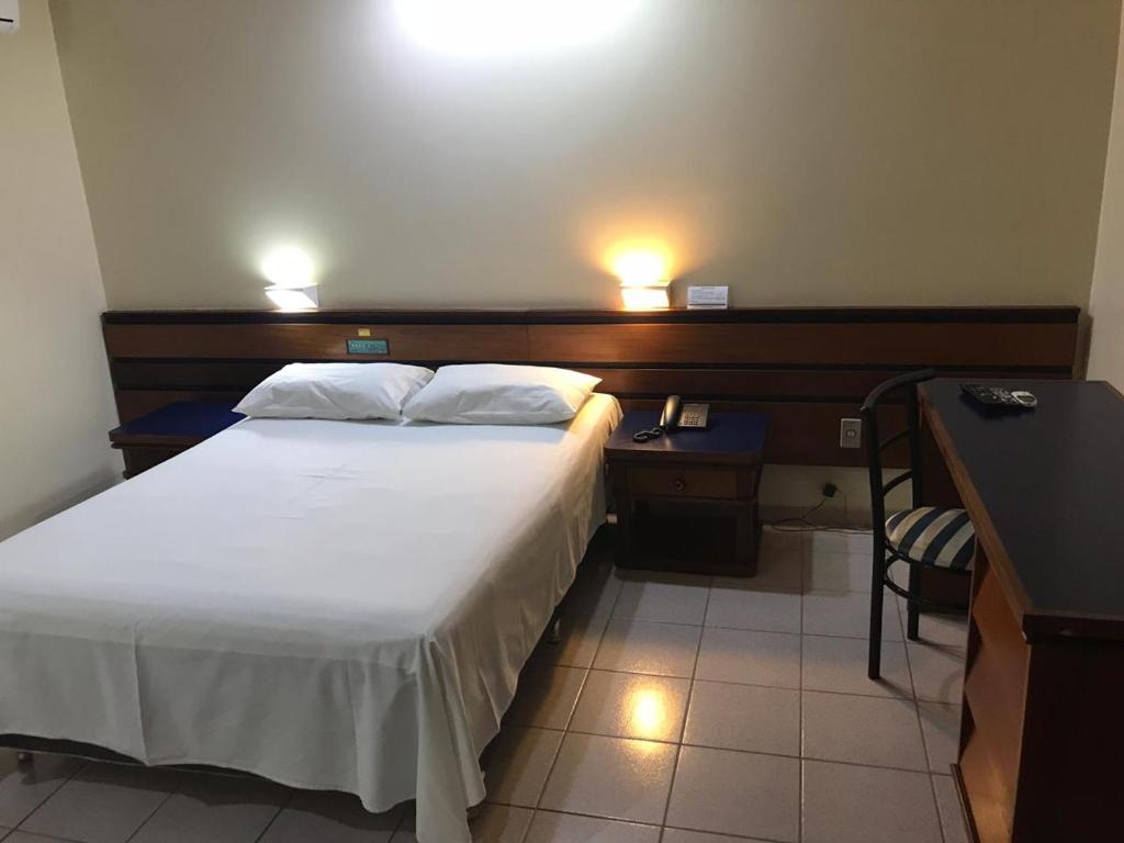 a bedroom with a bed and a desk with two lights at Oft Plaza Oeste Hotel in Goiânia