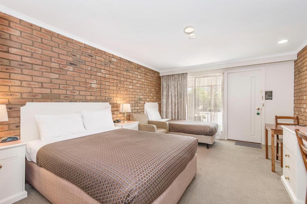 een slaapkamer met een bed en een bakstenen muur bij Golden Square Motor Inn in Bendigo