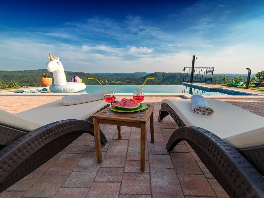 een patio met een tafel en 2 stoelen met wijnglazen bij Home Andrea with infinity salty pool in Roč