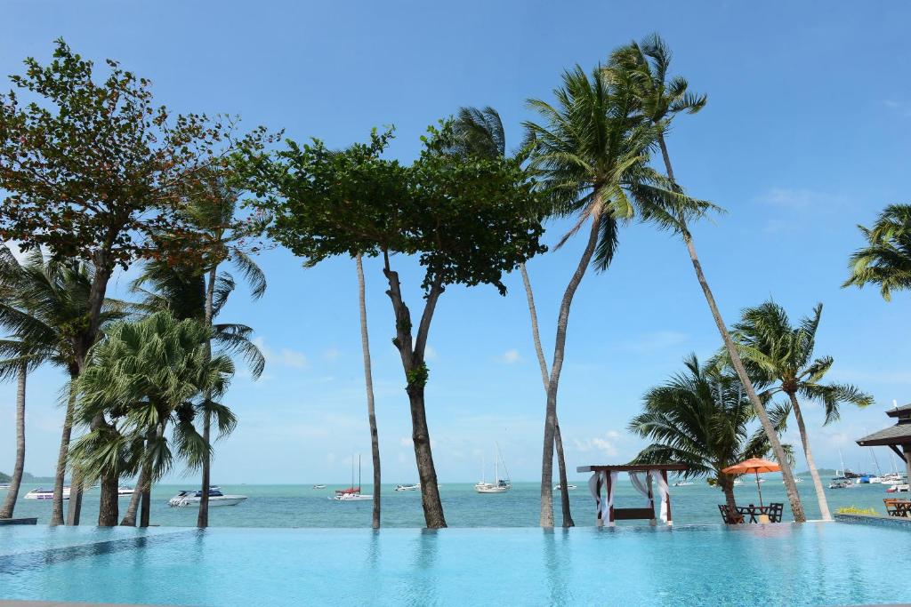 einen Pool neben einem Strand mit Palmen in der Unterkunft Samui Mermaid Beachfront in Bangrak Beach