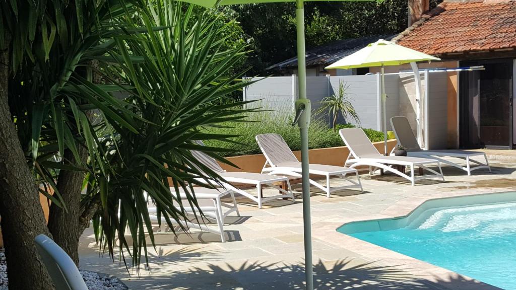 eine Gruppe Stühle und ein Sonnenschirm neben einem Pool in der Unterkunft Auberge de la Cauquiere in Le Beausset