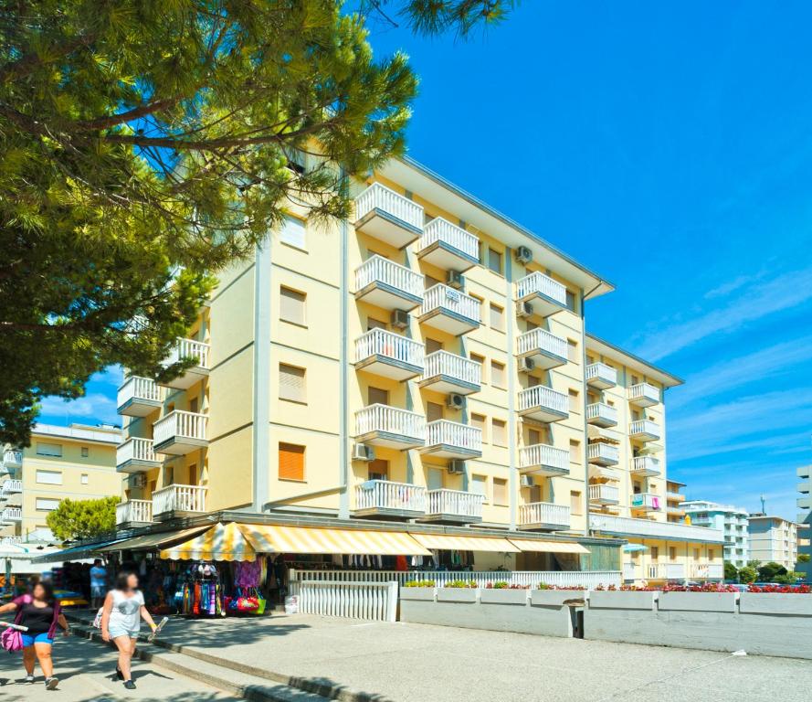 ein hohes Gebäude mit Balkonen und Menschen, die davor spazieren in der Unterkunft Ivana Belmare apartaments in Bibione