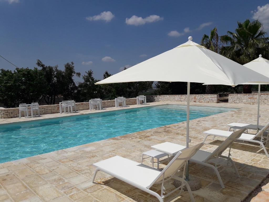 una piscina con sillas, una sombrilla y una piscina en Masseria La Gravina, en Palagianello