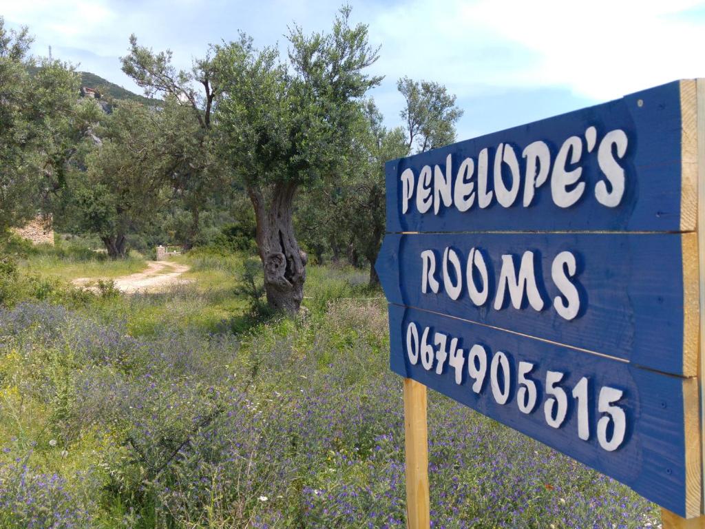 a blue sign in a field with a tree at Penelope's Rooms in Dhërmi