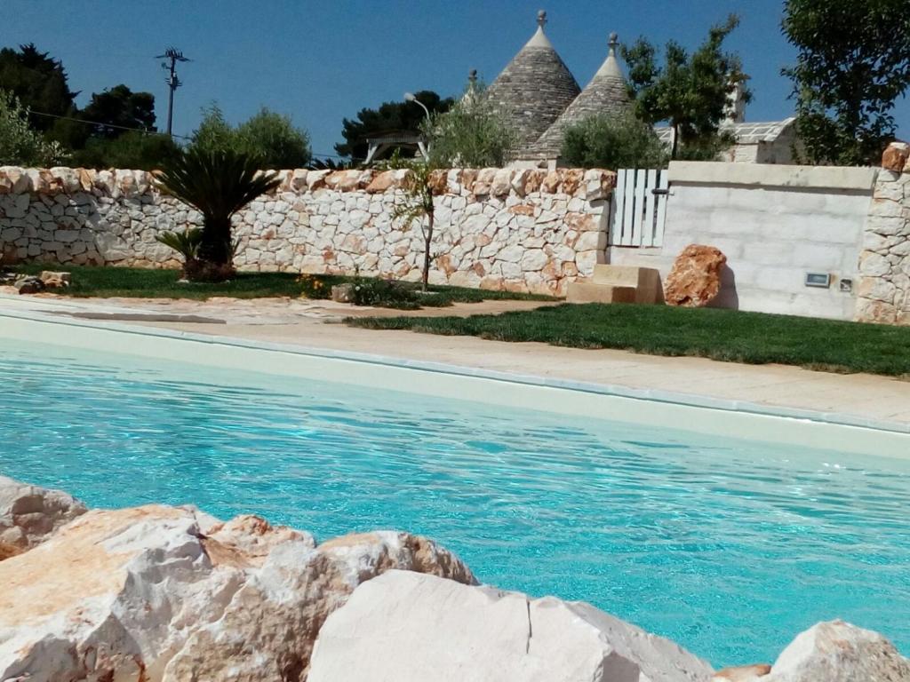 einen Pool mit blauem Wasser und einer Steinmauer in der Unterkunft Trulli La collinetta in Martina Franca