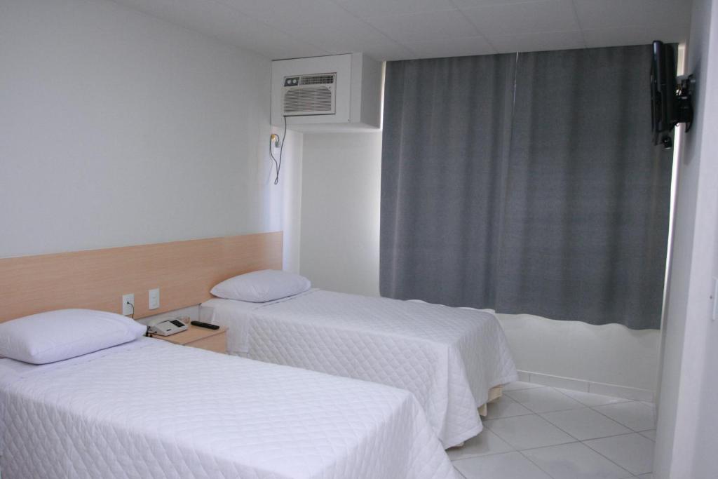 two beds in a room with white sheets and a window at Hotel Arezzu in Linhares