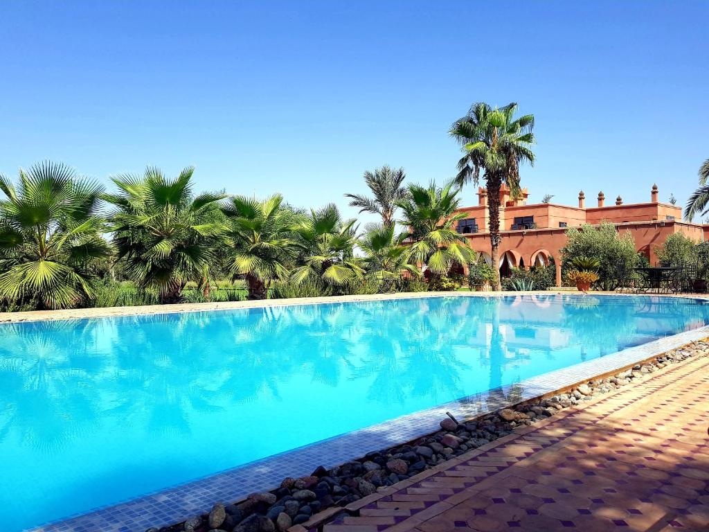 une grande piscine bordée de palmiers et un bâtiment dans l'établissement Ksar Salha, à Marrakech