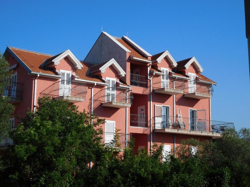 a large red building with balconies and trees at Apartments Sunrise in Tivat