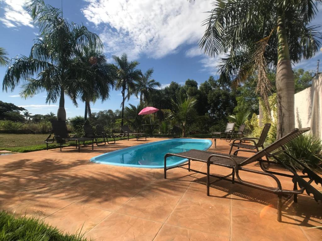 a pool with chairs and a table and palm trees at Pousada Recanto Flor de Lótus in Olímpia