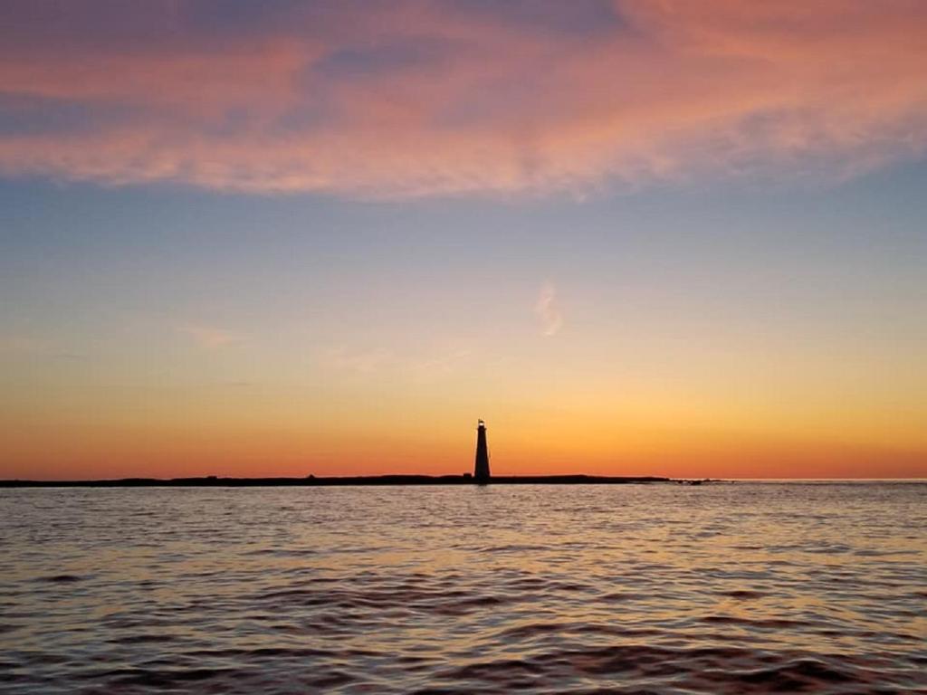 a lighthouse in the middle of the water at sunset at Mama`s By The Sea B&B in Clark's Harbour
