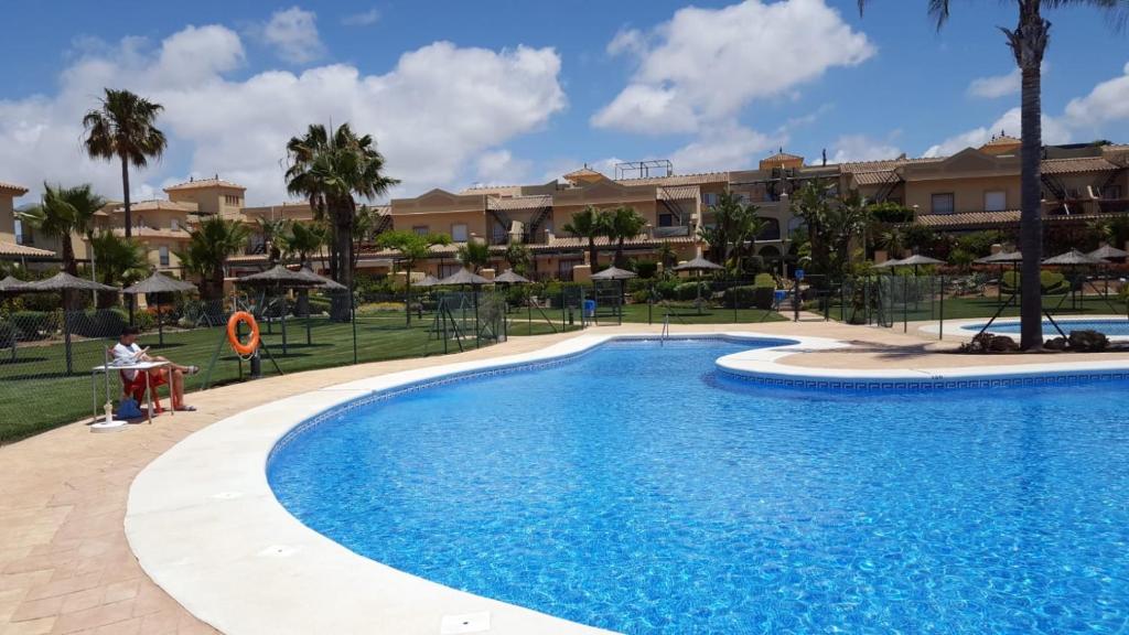 ロタにあるApartamento Costa Ballenaのヤシの木と建物が並ぶリゾートのプールを利用できます。