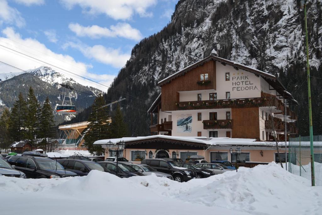 een groot gebouw met auto's geparkeerd in de sneeuw bij Parkhotel Fedora in Campitello di Fassa