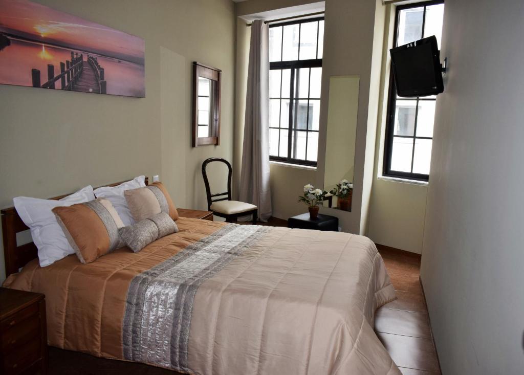 a bedroom with a bed with a television and two windows at GuestHouse Belo Horizonte in Porto