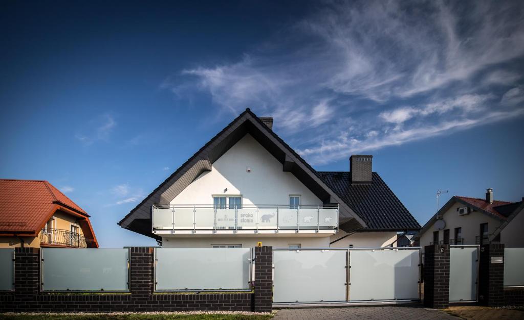 a white house behind a fence with a balcony at Pensjonat Spoko Słonia w Rewalu in Rewal