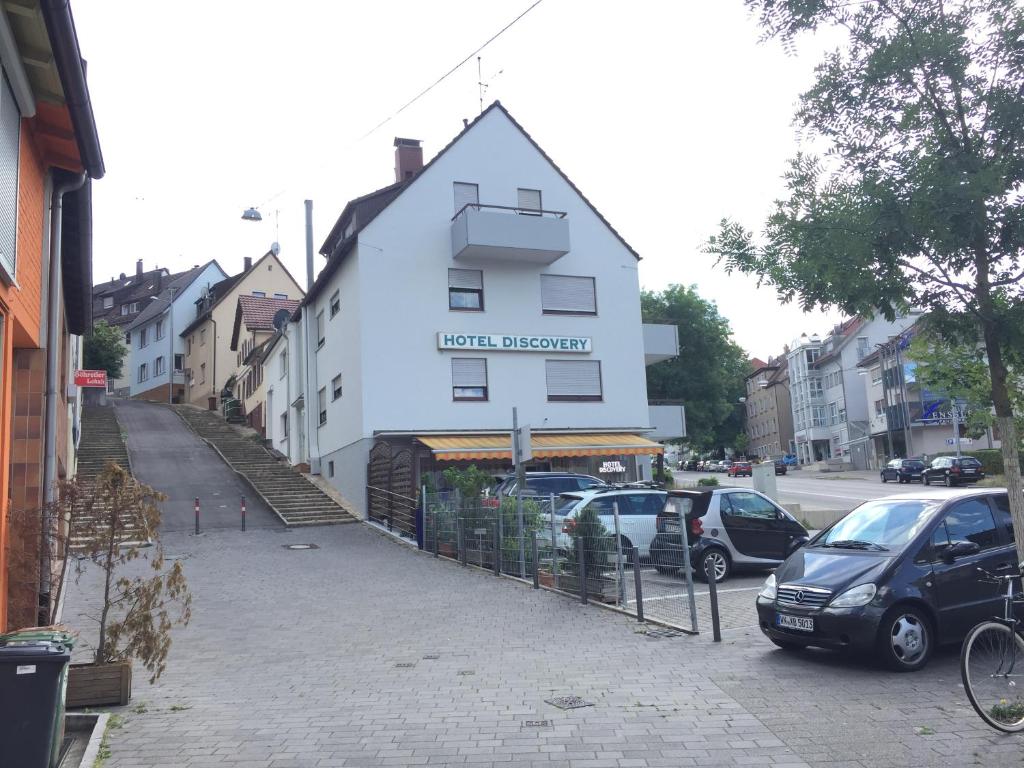 ein weißes Gebäude auf einer Straße mit geparkten Autos in der Unterkunft Hotel Discovery in Stuttgart