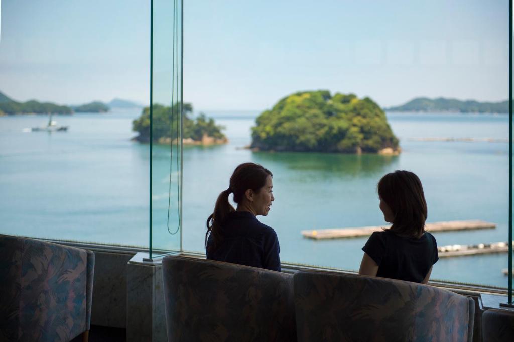 two women sitting in a room looking out at an island at Toba Grand Hotel in Toba