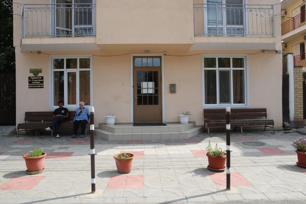 dos personas sentadas en bancos frente a un edificio en Bereg Anapy Guest House en Anapa