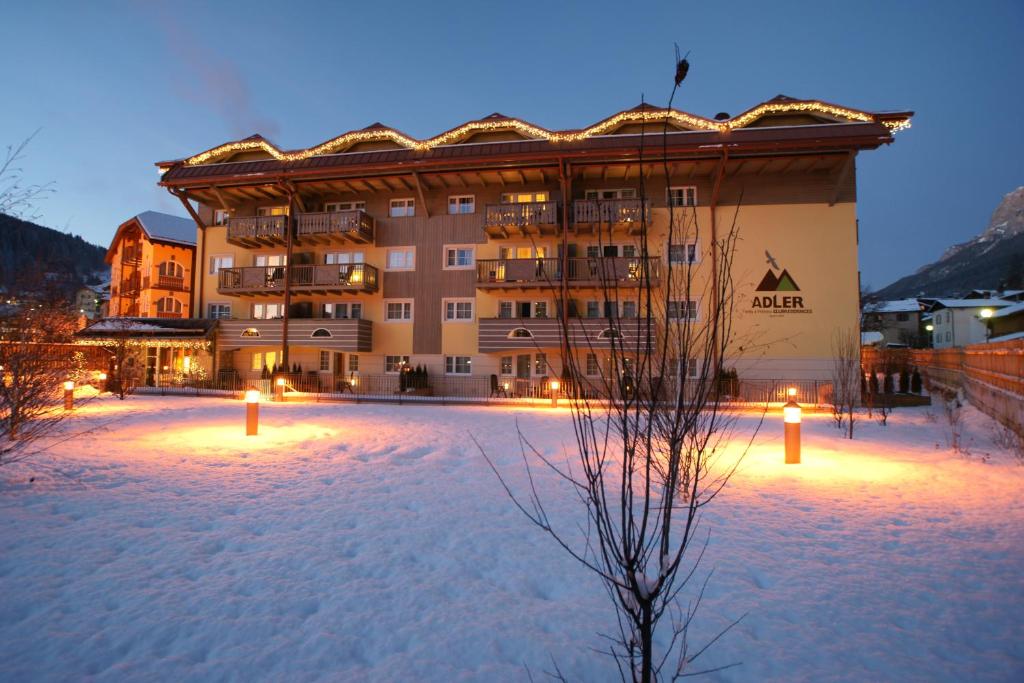 un grand bâtiment avec des lumières dans la neige la nuit dans l'établissement Adler ClubResidence, à Moena