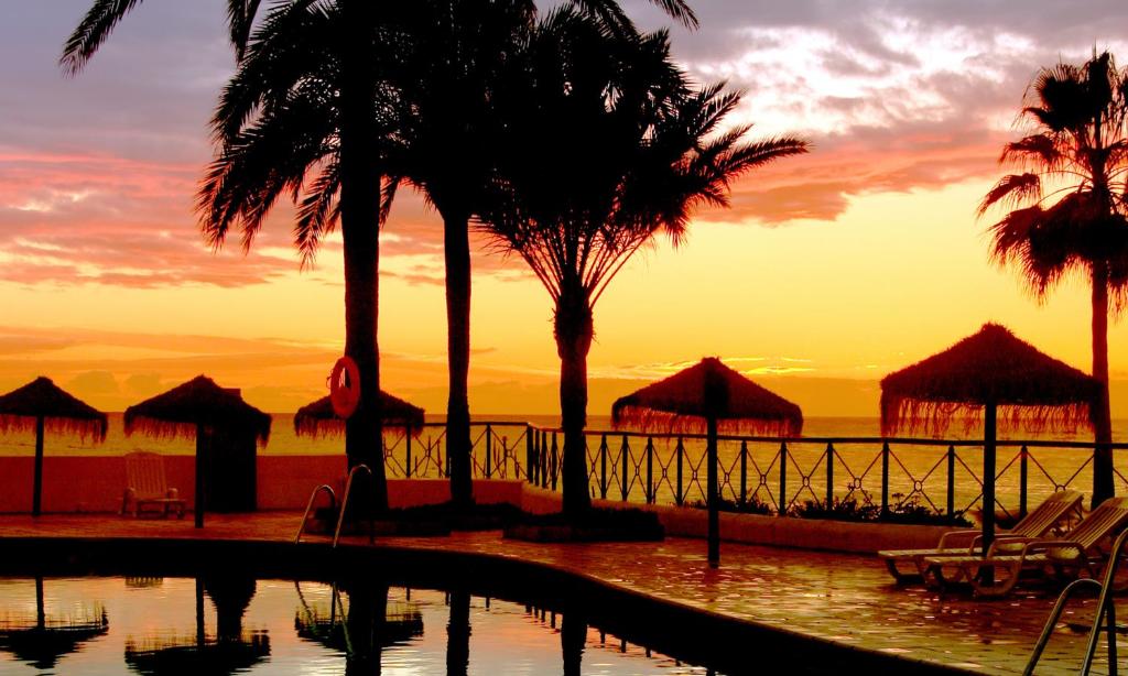 a sunset at a resort with palm trees and a pool at Macdonald Doña Lola Resort in La Cala de Mijas