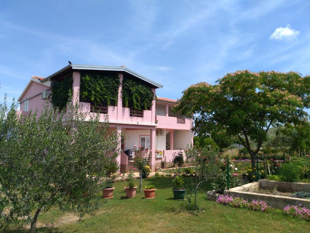 une maison rose avec des plantes dans la cour dans l'établissement Apartment Ema, à Posedarje