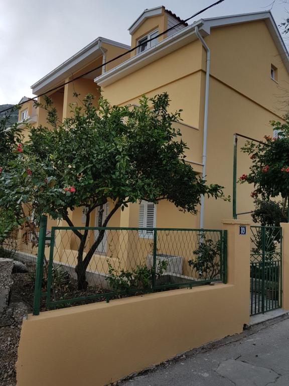 a yellow house with a fence and a tree at Apartments Viganj in Viganj