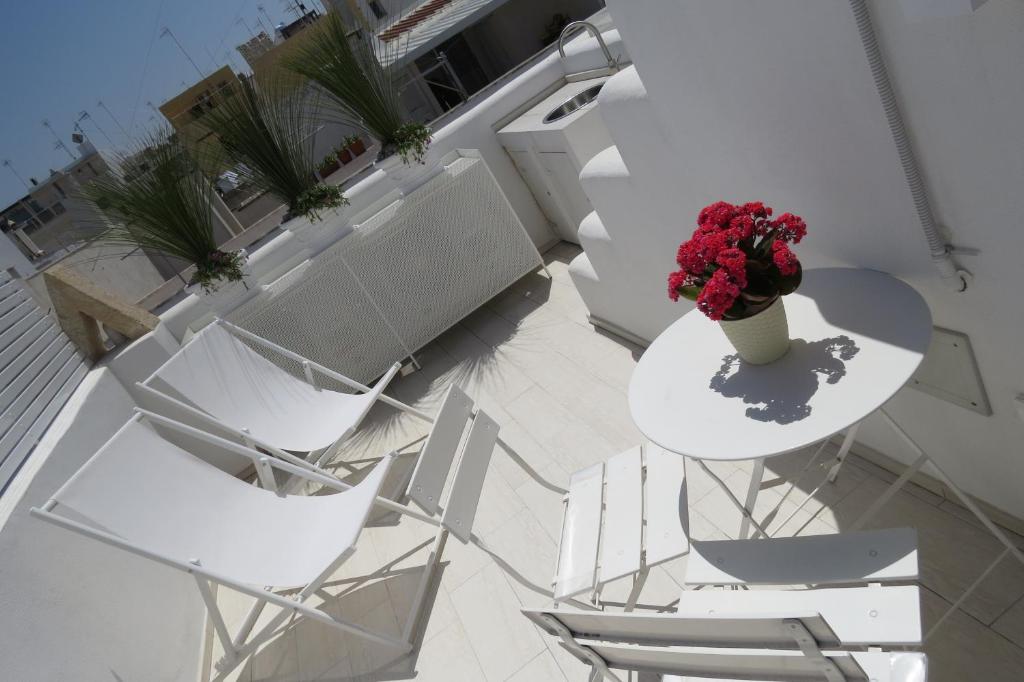 un balcone con sedie bianche e un tavolo con un vaso di fiori di Sirenè a Polignano a Mare