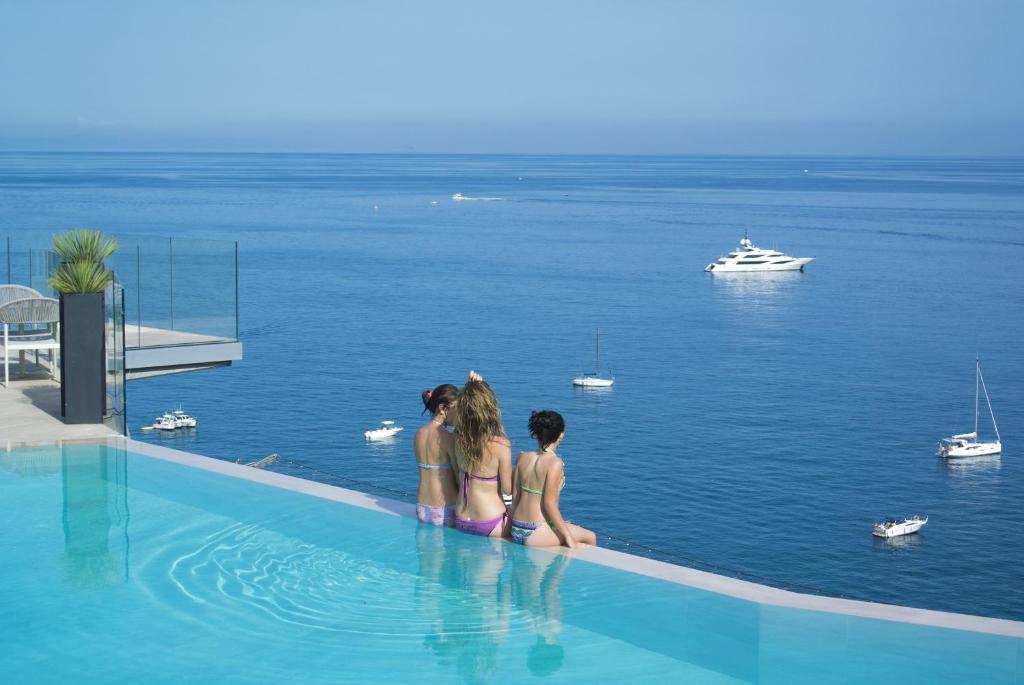 Dos chicas y un chico sentados en una piscina con vistas al agua en B&B Capo Torre Resort & SPA, en Albisola Superiore