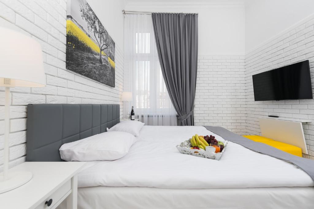Bright modern bedroom with large bed, fruit tray, tall gray curtains and wall-mounted TV.