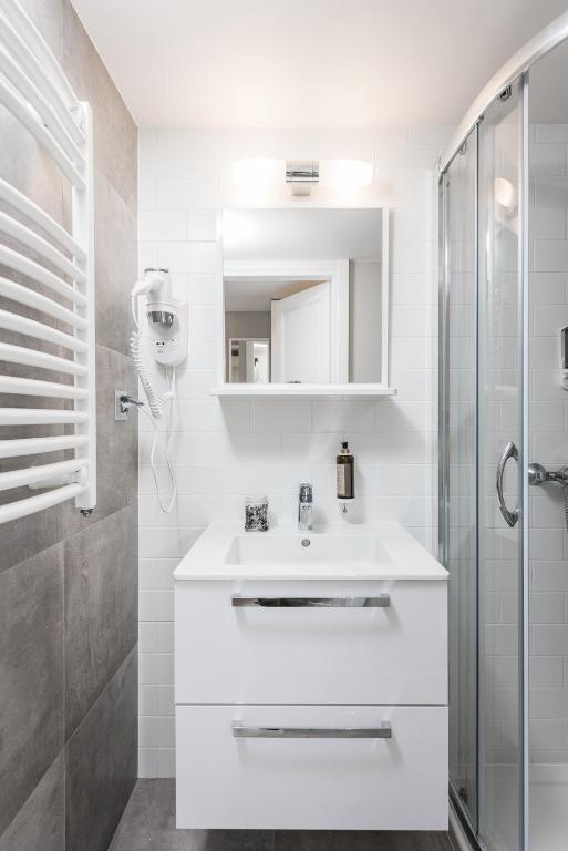 Compact white bathroom vanity with mirror, wall-mounted hairdryer, clean tiled walls, bright lighting