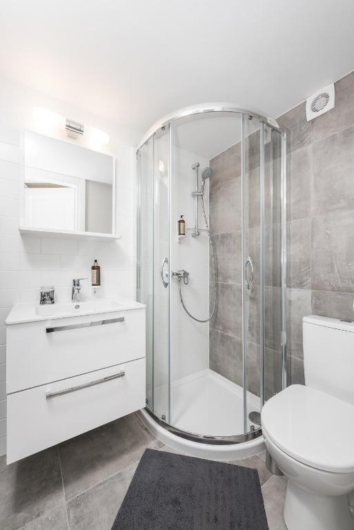 Modern bathroom featuring curved glass shower, white vanity, toilet, gray tile flooring
