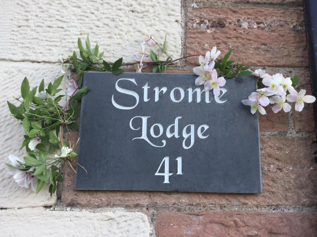 a sign on the side of a brick wall with flowers at Strome Lodge in Inverness
