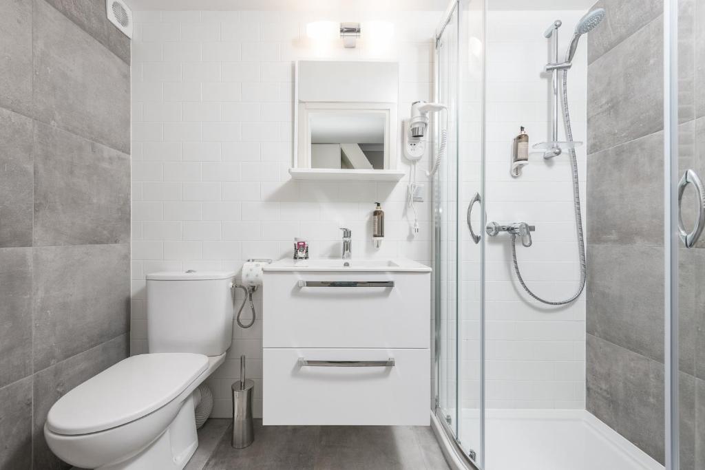 Bright white and gray bathroom with sink vanity, toilet, glass shower, minimalist fixtures
