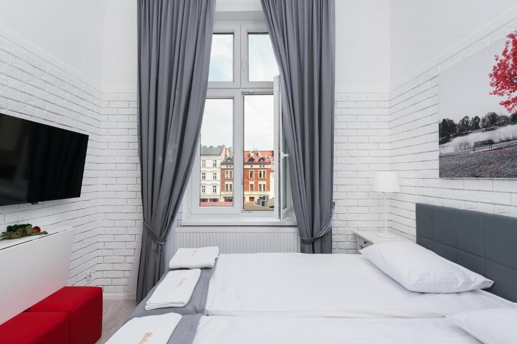 Bright white bedroom with twin beds, gray curtains framing window showing city buildings.
