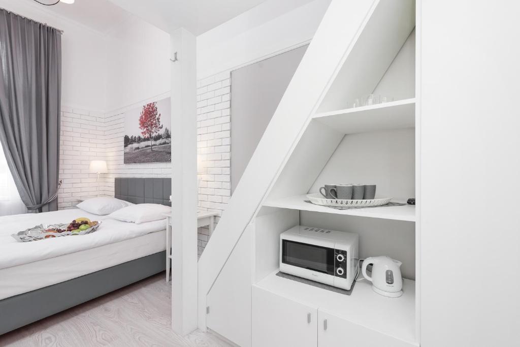 Compact bedroom corner with bed beside angled shelving unit containing microwave, kettle and cups.