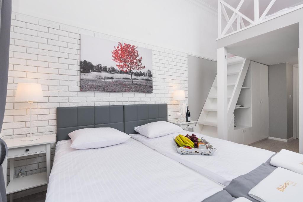 Twin beds in bright white room with loft stairs, fruit tray, lamps, red tree wall art