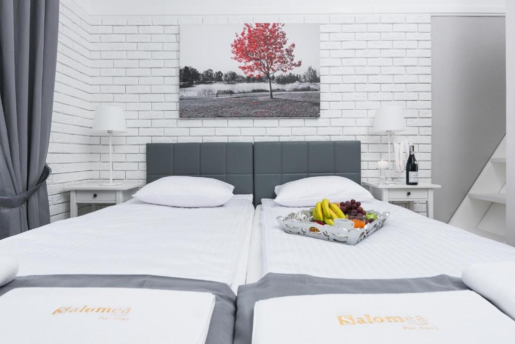 Two single beds pushed together with fruit breakfast tray, red tree artwork and bedside lamps.