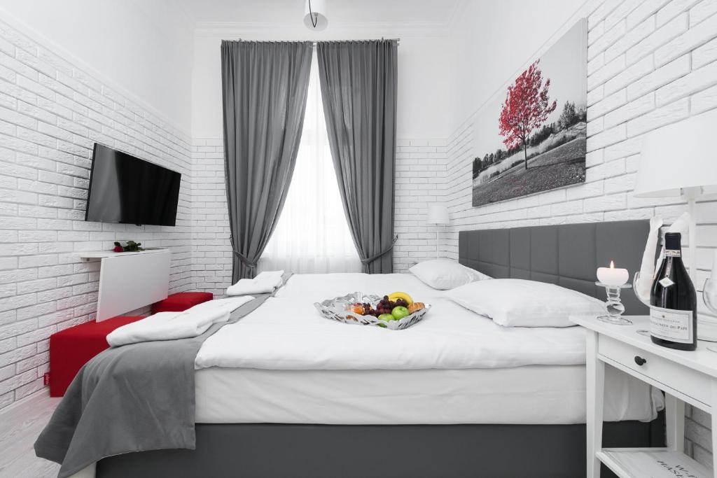 Bright bedroom with central double bed, gray curtains, fruit platter, wall-mounted TV and white brick walls.