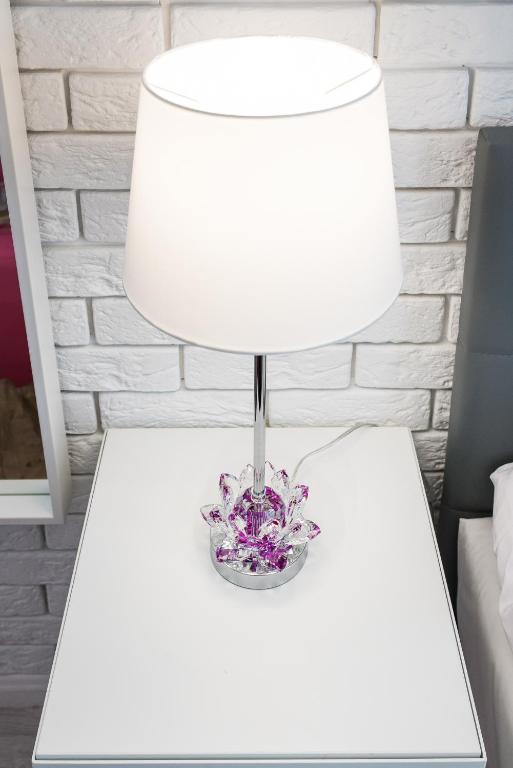White bedside lamp with decorative crystal base on a minimalist white nightstand against brick wall.