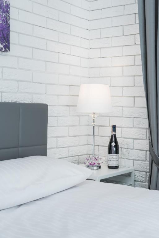 Bedside scene with lit lamp, wine bottle on white side table, gray headboard and white bedding.