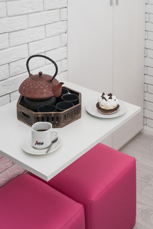 Red cast-iron teapot, coffee cup and dessert on white table beside bright pink stools, cozy corner.