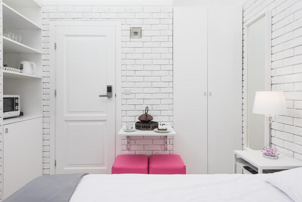 White entry area with built-in shelves, microwave, kettle, small table, and two bright pink ottomans.